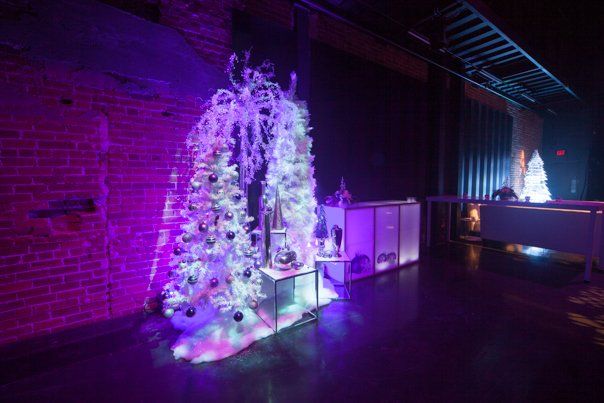 A christmas tree is lit up in a dark room with purple lights.