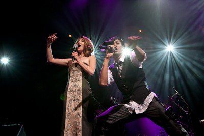 A man and a woman are singing into microphones on a stage.