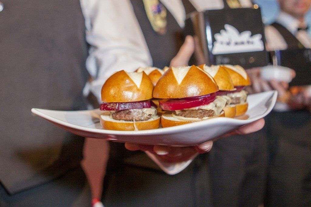 A person is holding a plate of sliders on a white plate.