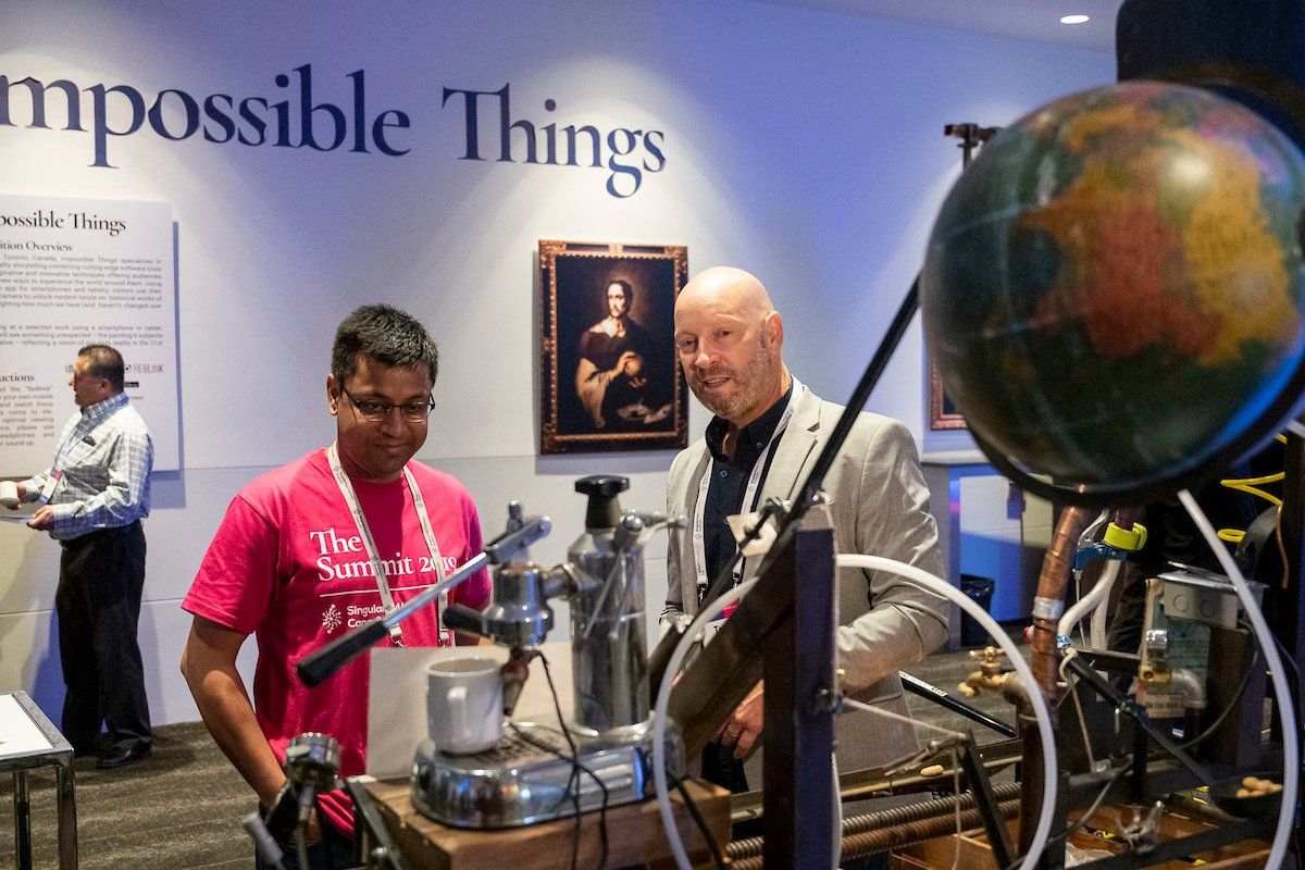 Two men are looking at a machine in front of a wall that says impossible things
