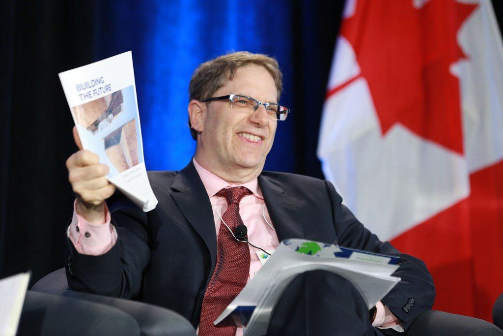 A man in a suit and tie is holding a book in front of a canadian flag