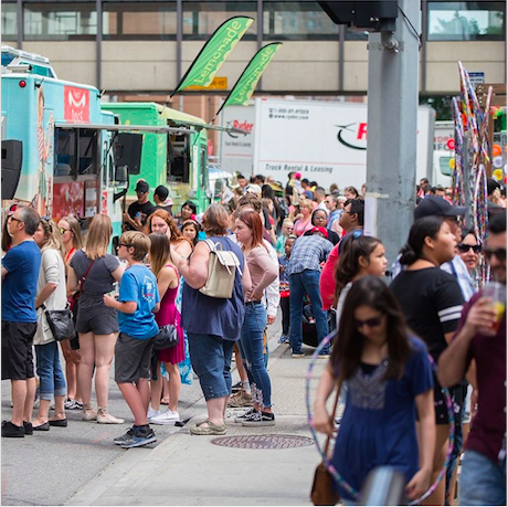 A crowd of people are gathered on the sidewalk in front of food trucks