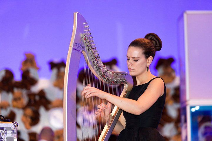 A woman in a black dress is playing a harp on a stage.