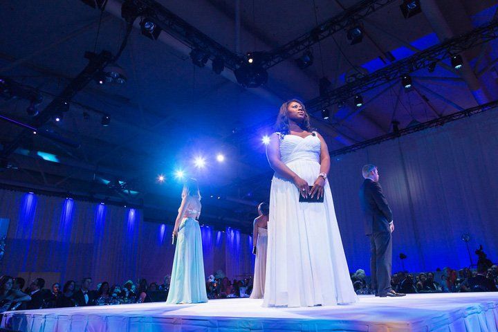 A woman in a white dress is standing on a stage at a fashion show.