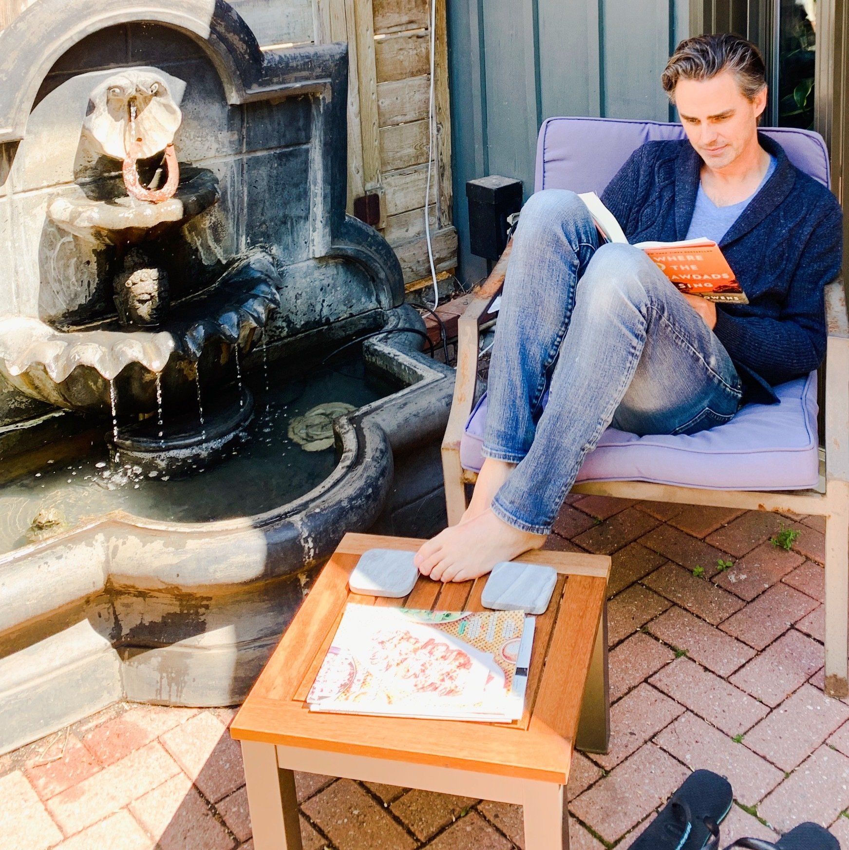 A man sits in a chair reading a book in front of a fountain
