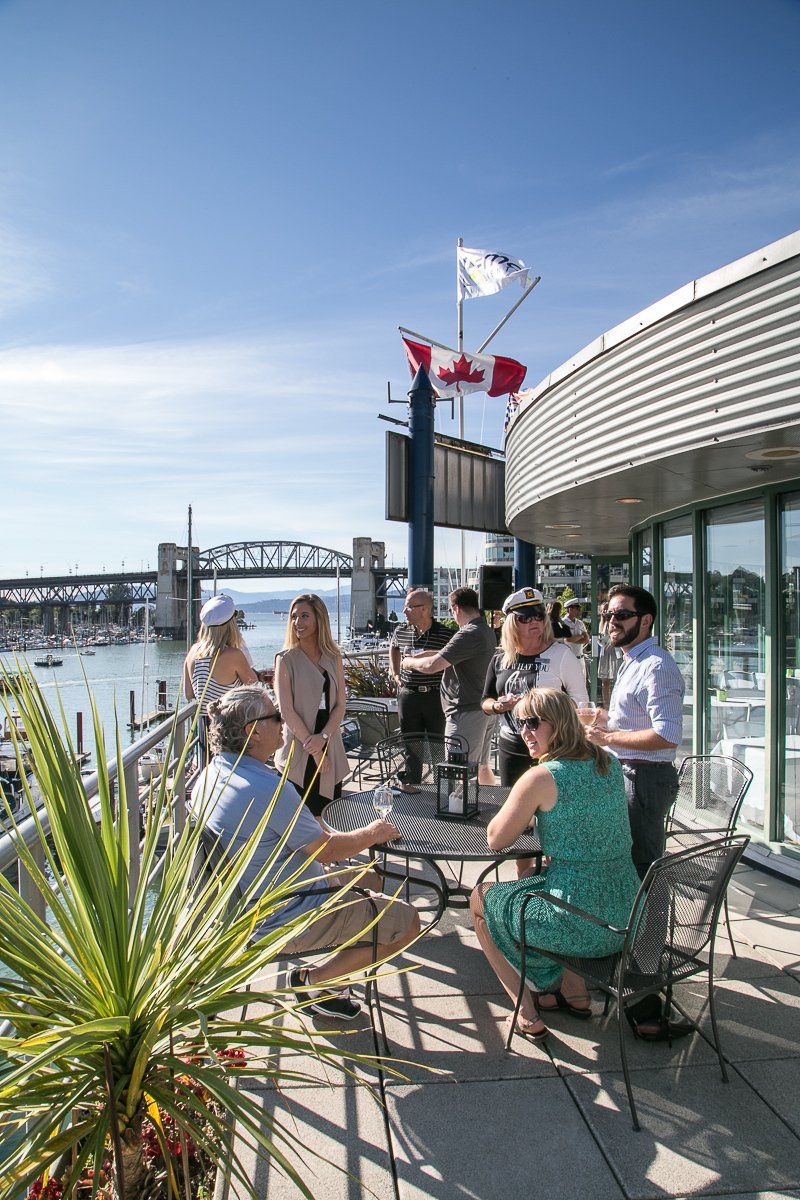 A group of people are sitting at tables on a balcony overlooking a body of water.