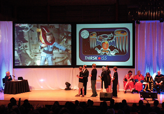 A group of people standing on a stage in front of a screen that says tmrsk iss