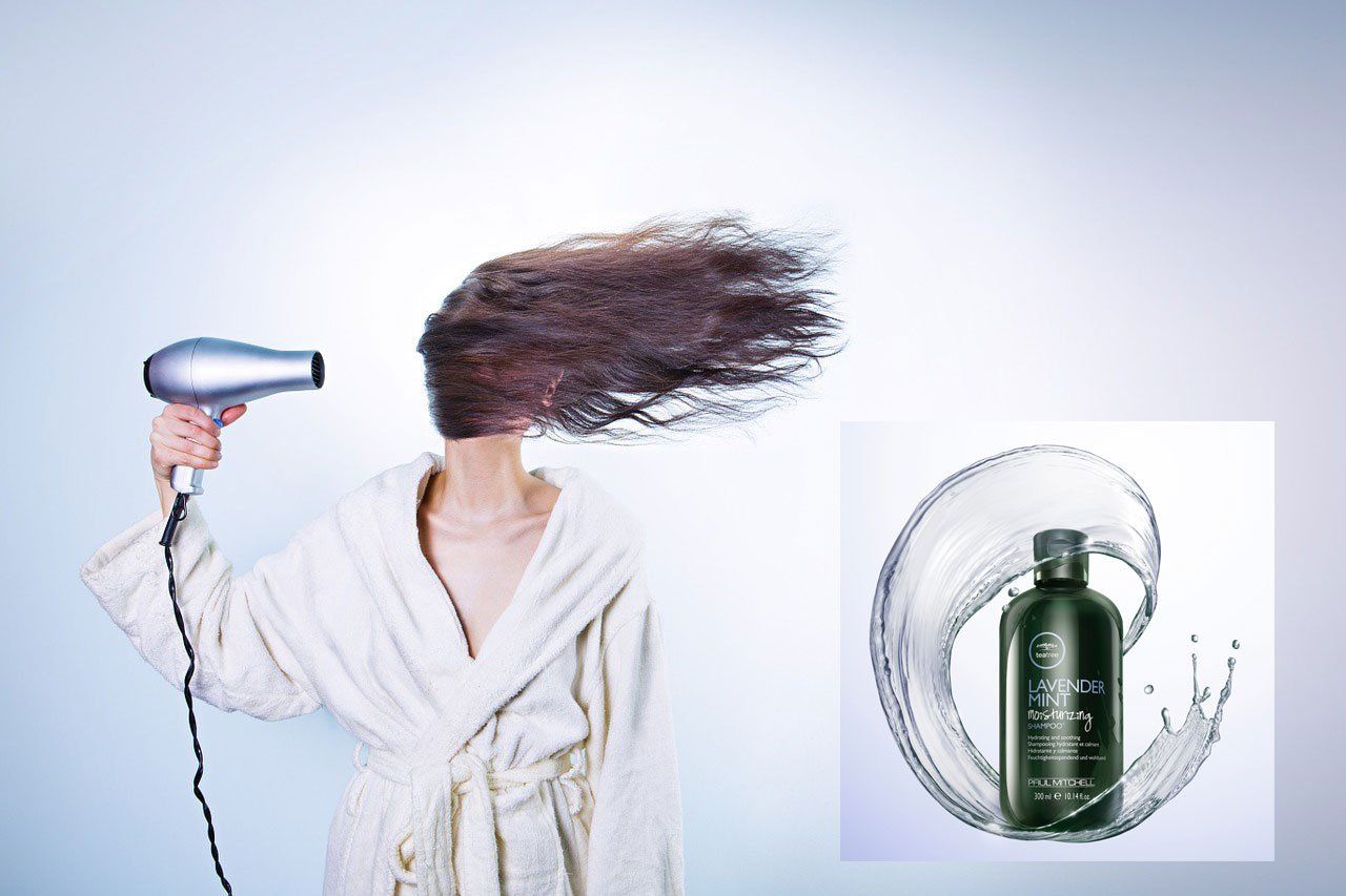 Person in bathrobe blow-drying hair. Shampoo bottle with water splash in the corner.