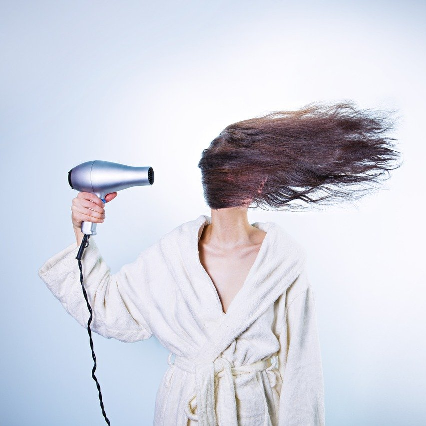 Person in white robe drying hair with silver hair dryer, hair blowing wildly.