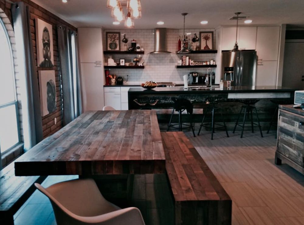 Rustic kitchen and dining area with wooden table, bench, and bar stools. Bright, open layout.