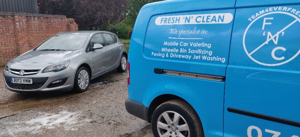 sign written business van parked up next to car