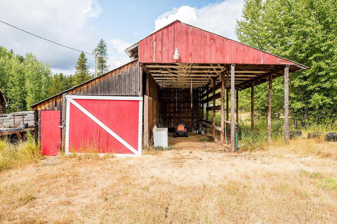 Red barn with open-sided structure, weathered wood, and a red door, set in a field with trees under a cloudy sky.