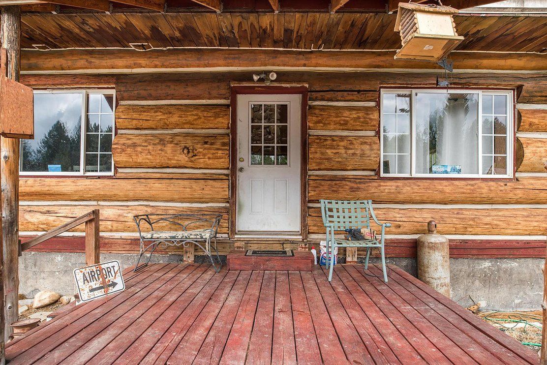 Wooden cabin porch with a red-painted deck, white door, two windows, and a green chair.
