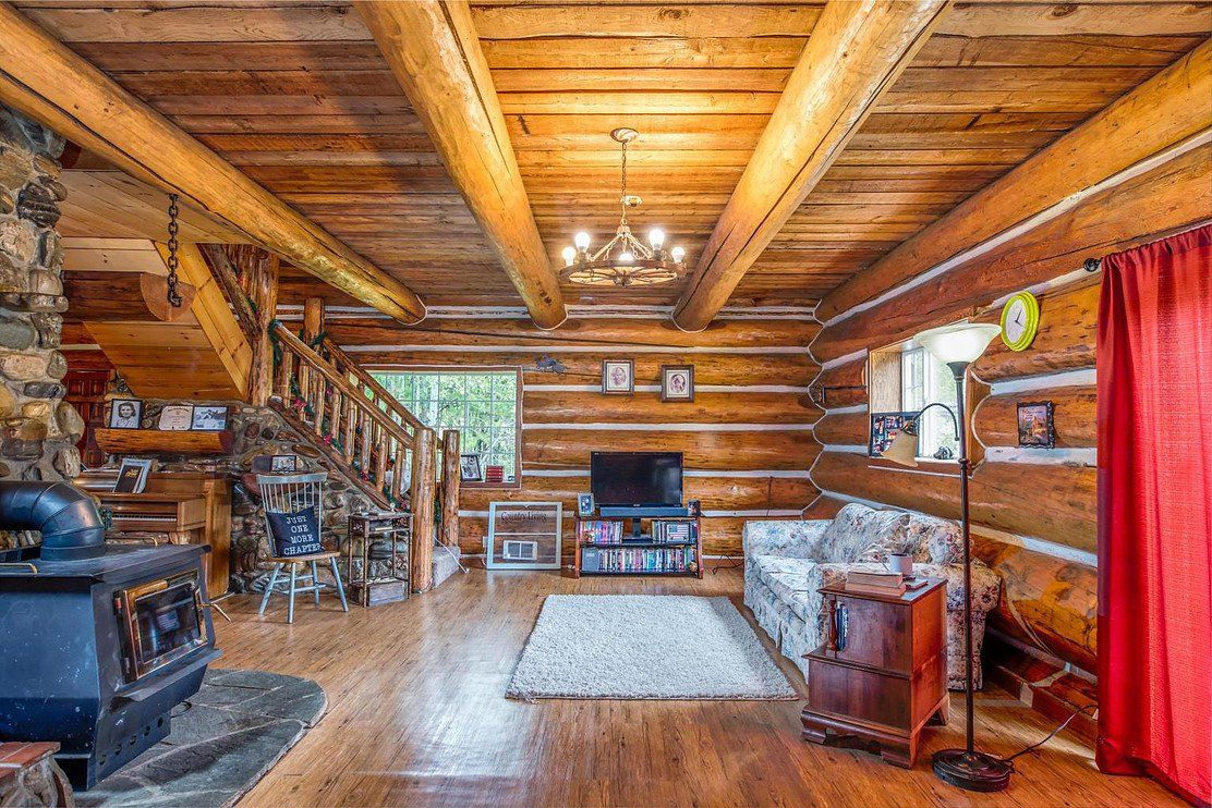 Cozy log cabin living room with exposed beams, fireplace, and rustic decor. Includes a staircase, TV, and window with natural light.
