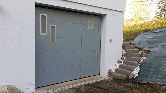 Porte de garage gris bleu avec regards verre et accès piéton réalisation Trihome