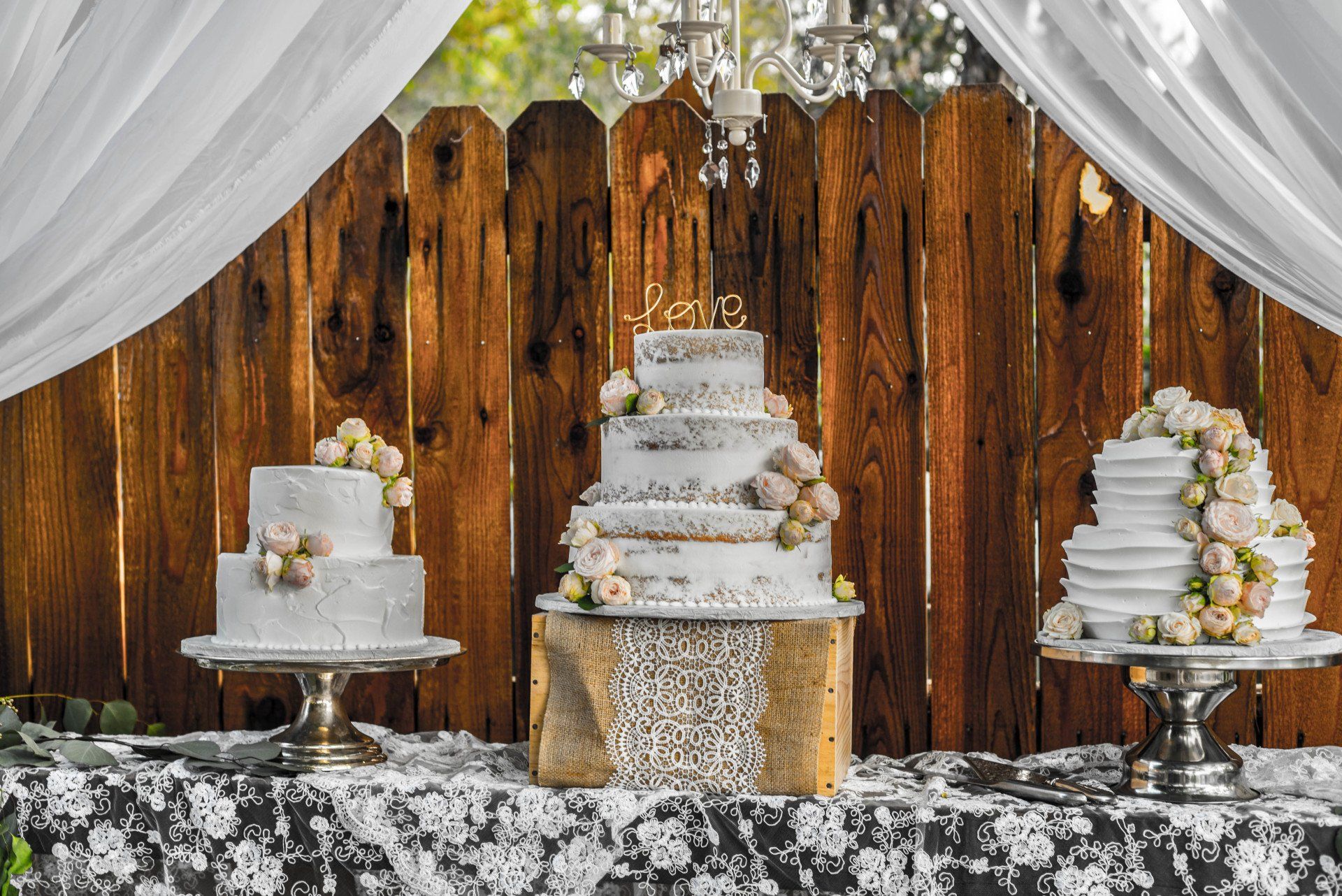 Three wedding cakes are sitting on a table in front of a wooden fence.