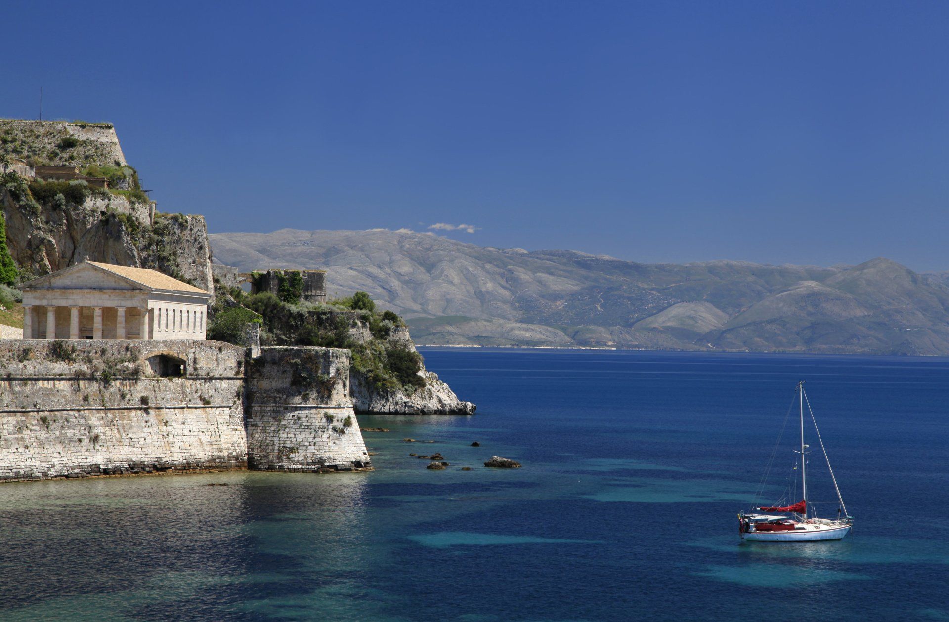 A sailboat is floating in the ocean near a cliff.
