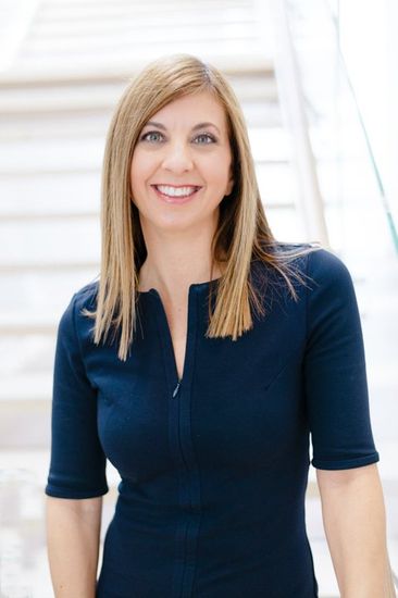A woman in a blue dress is smiling and standing in front of a set of stairs.