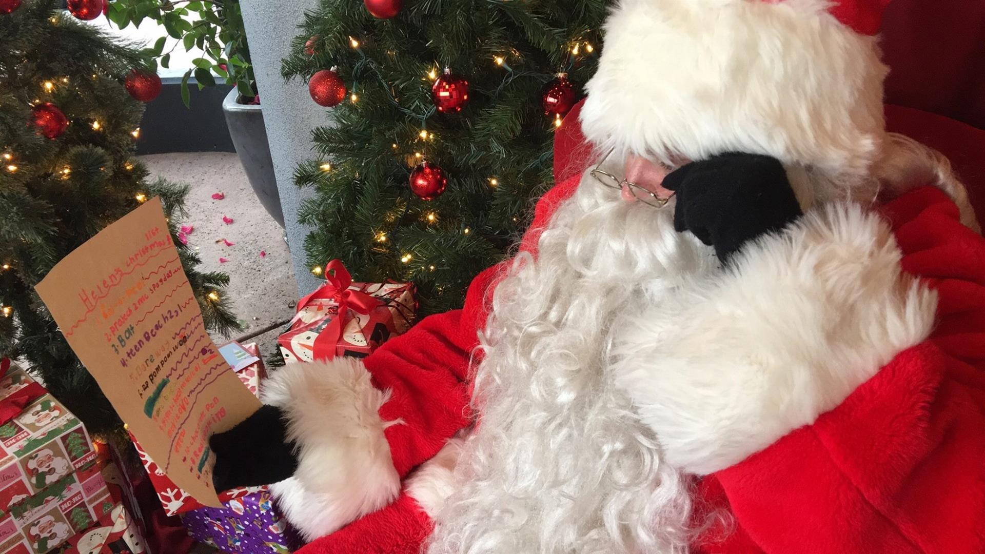 Santa claus is sitting in front of a christmas tree reading a letter from a child.
