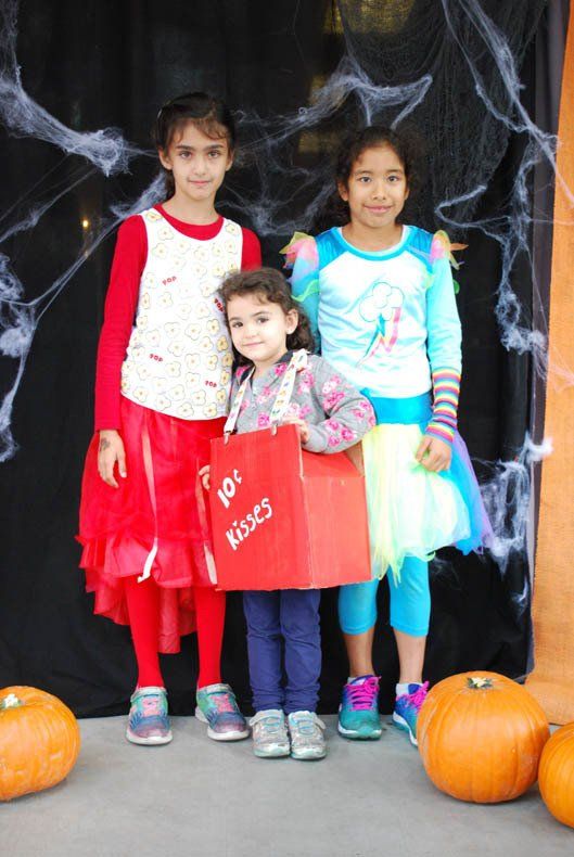 Three little girls are posing for a picture with pumpkins in the background
