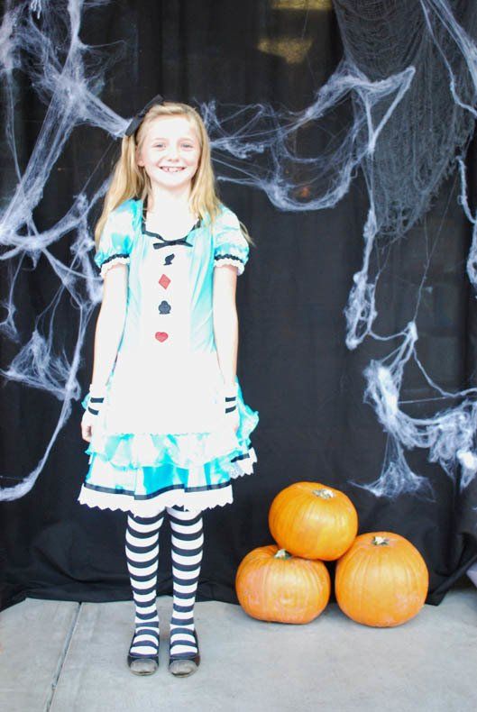 A little girl dressed as alice in wonderland stands in front of pumpkins