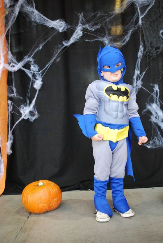 A young boy in a batman costume is standing next to a pumpkin.