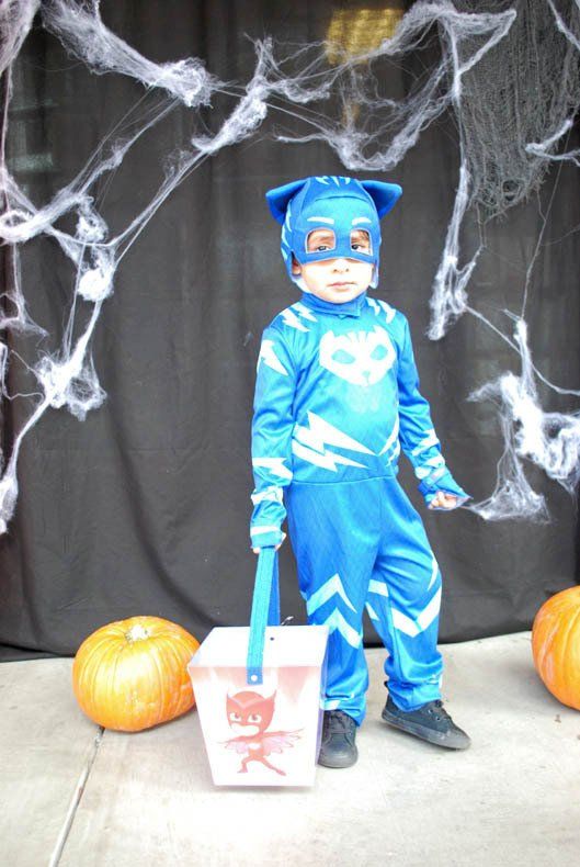 A young boy in a blue costume is holding a trick or treat bucket.