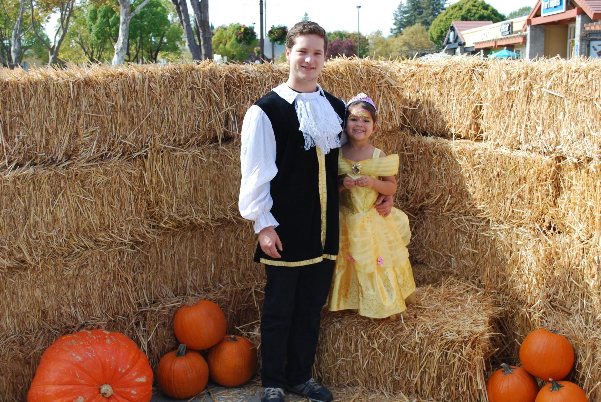 A man and a girl are posing for a picture in front of hay bales and pumpkins
