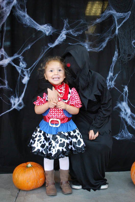 A little girl in a cowboy costume is posing for a picture with a grim reaper.