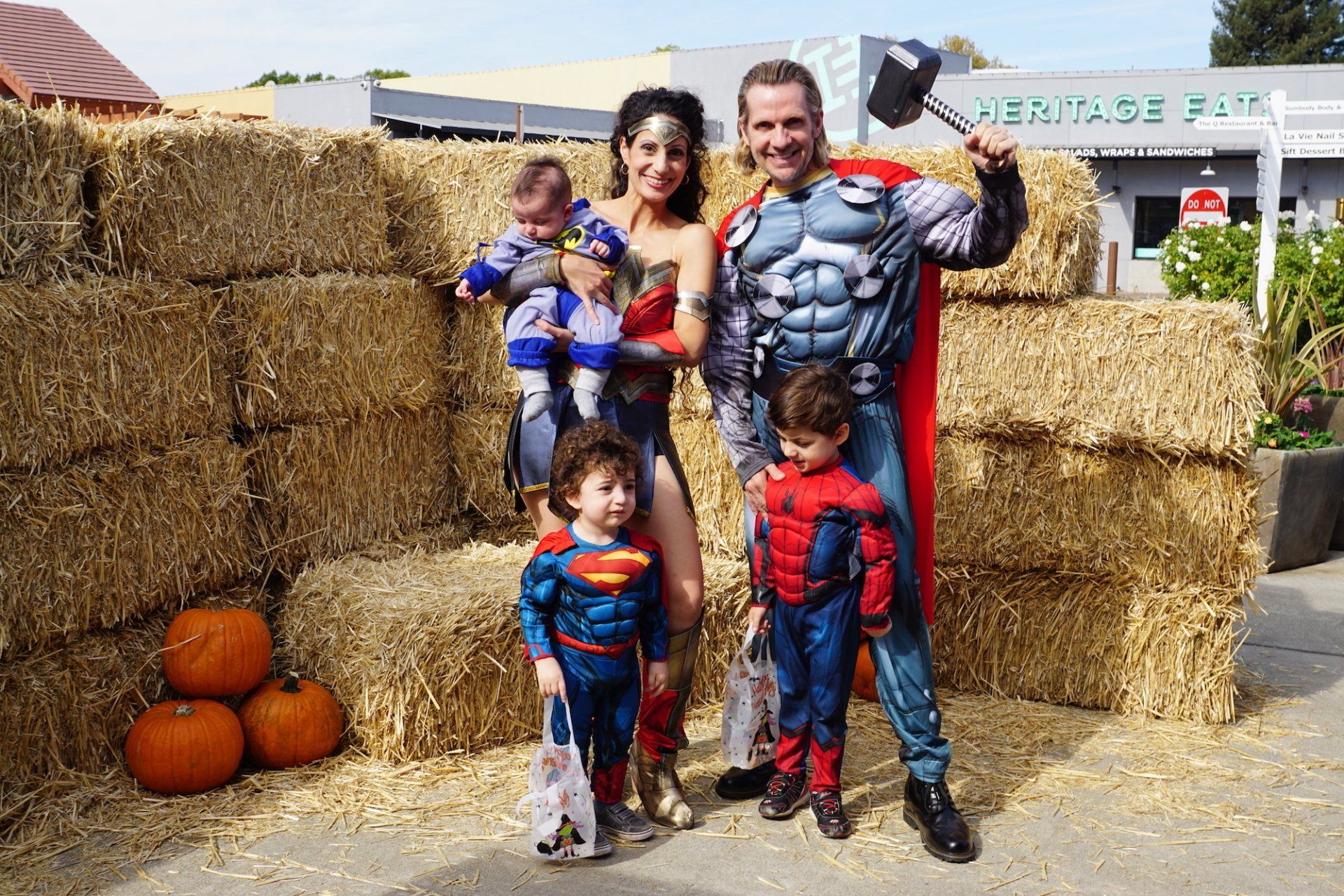 A family dressed in superhero costumes are posing for a picture in front of hay bales.