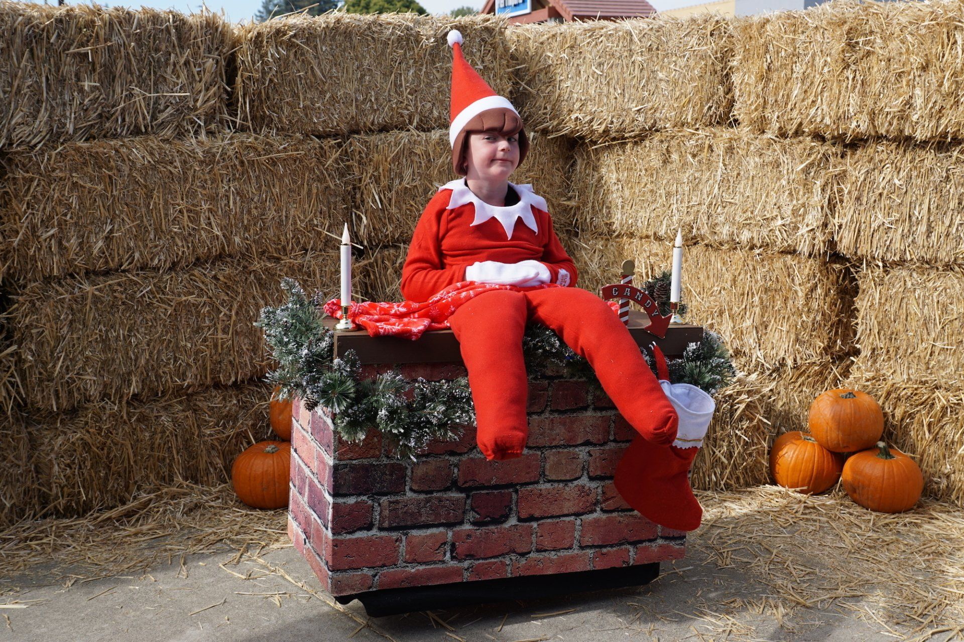 A person dressed as an elf on the shelf is sitting on a brick wall.