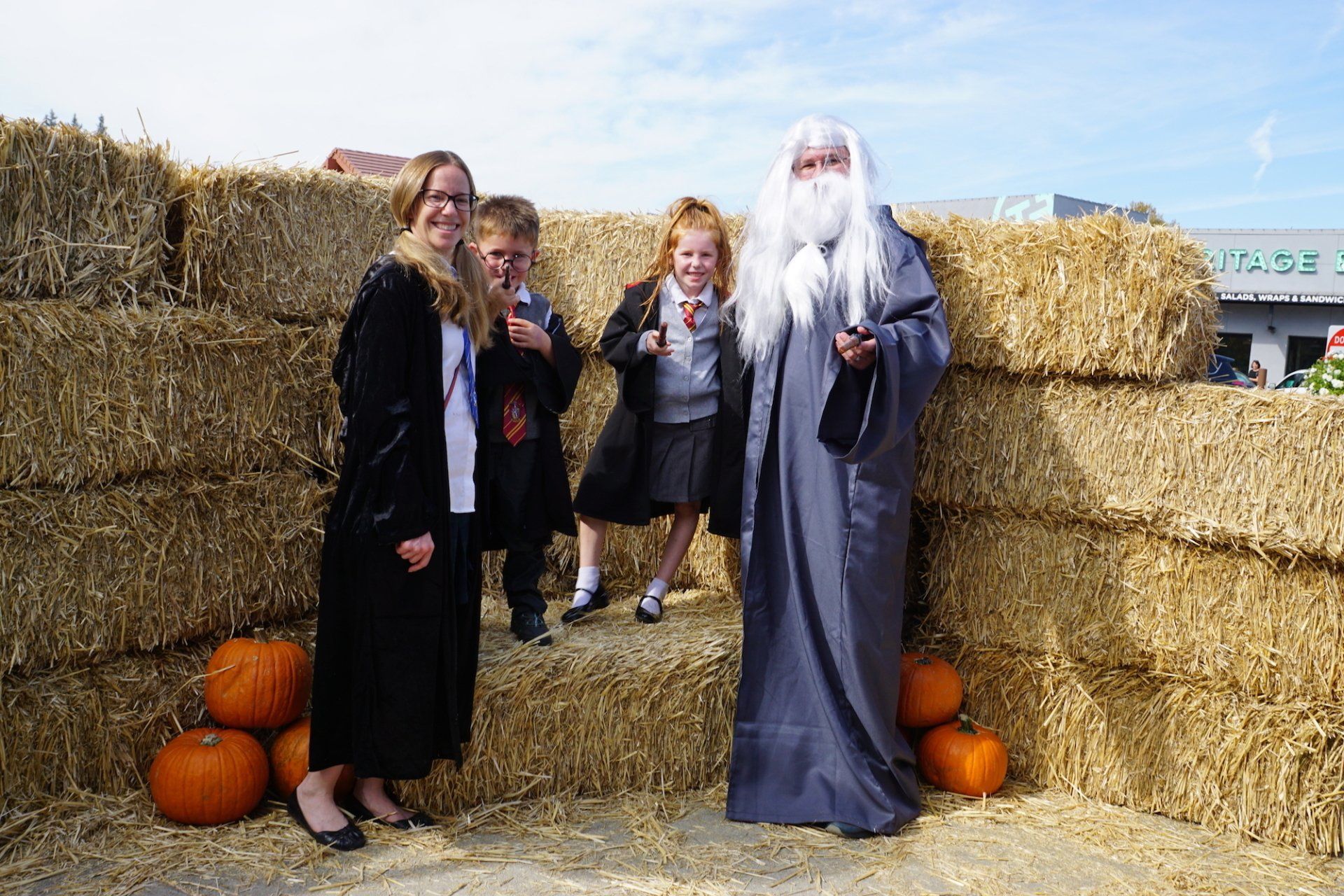 A group of people dressed as harry potter are standing next to hay bales and pumpkins.