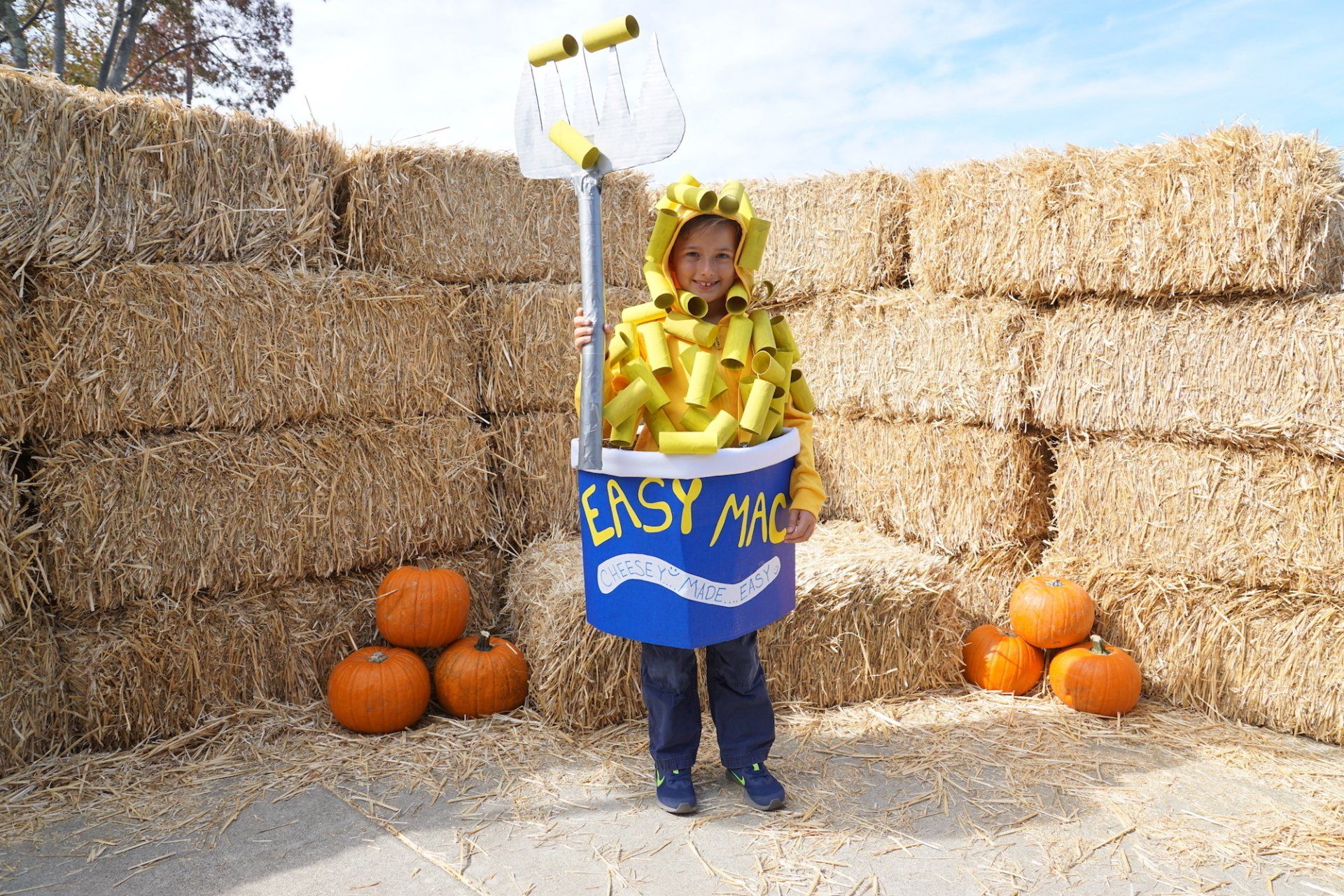 A child in an easy mac costume stands in front of hay bales and pumpkins
