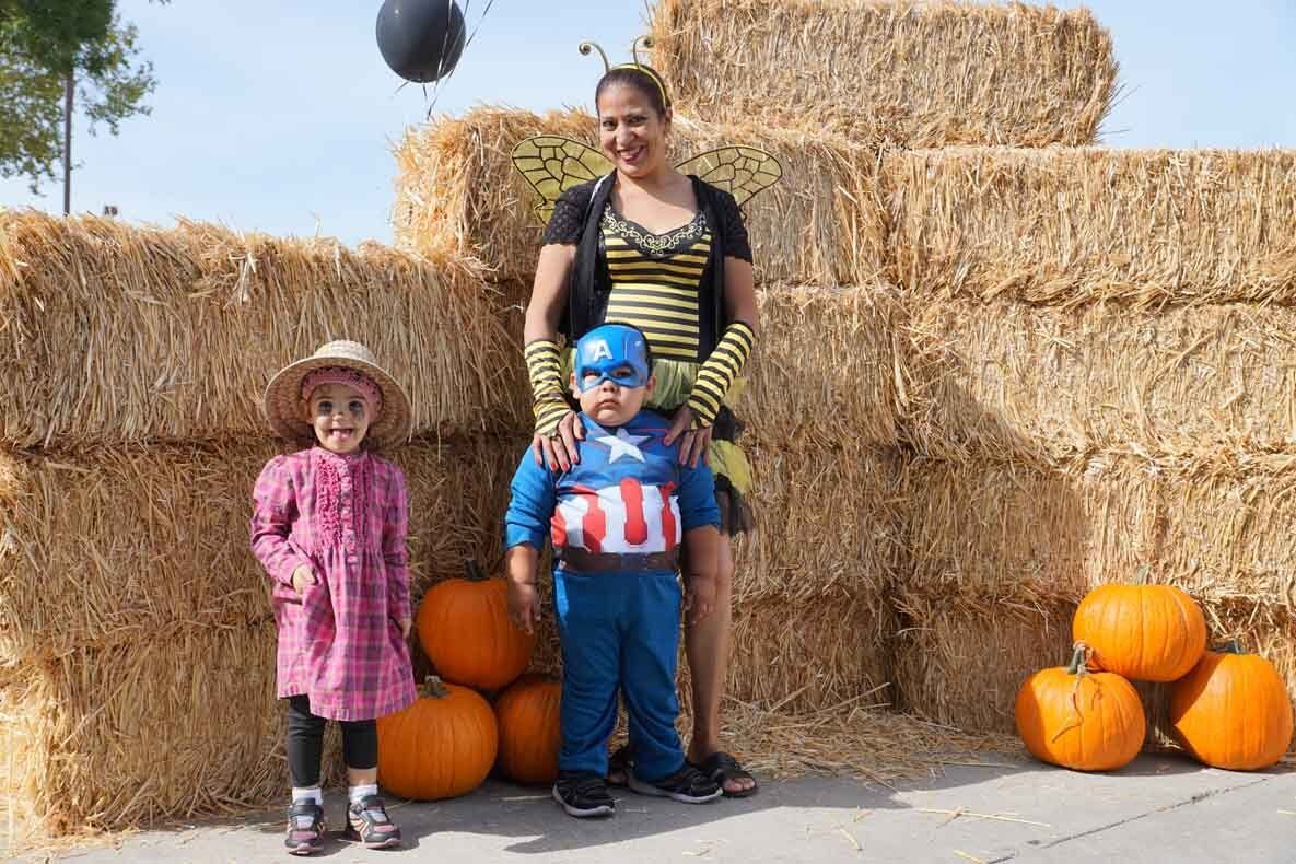 A woman and two children are posing for a picture in front of hay bales and pumpkins.