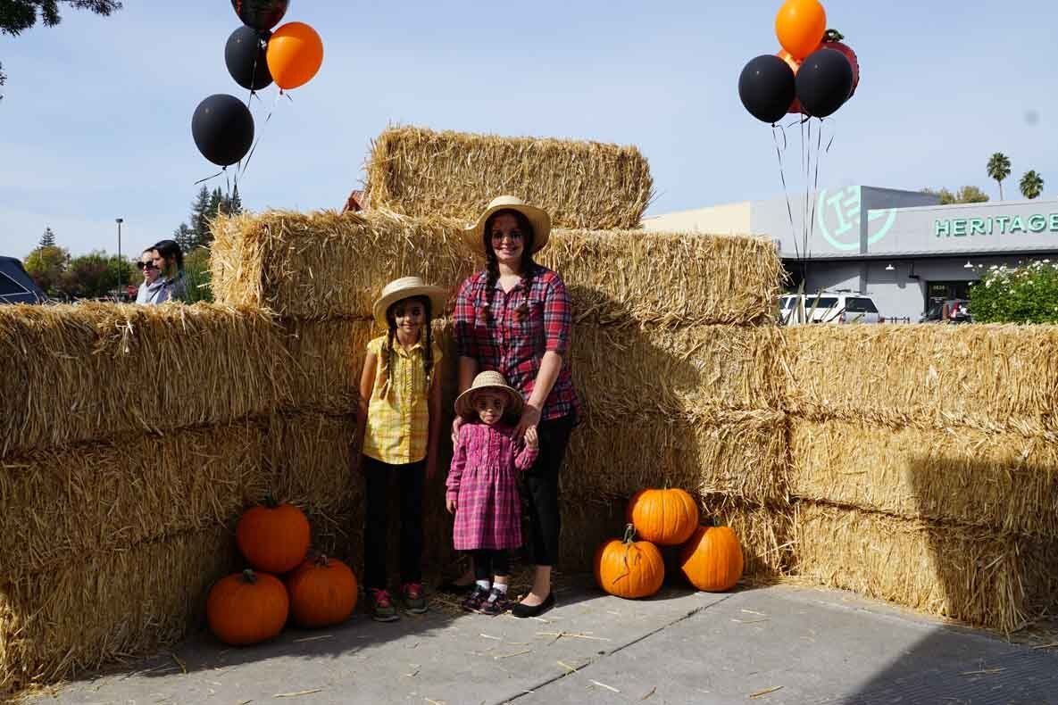 A woman and two children are standing next to hay bales and pumpkins.