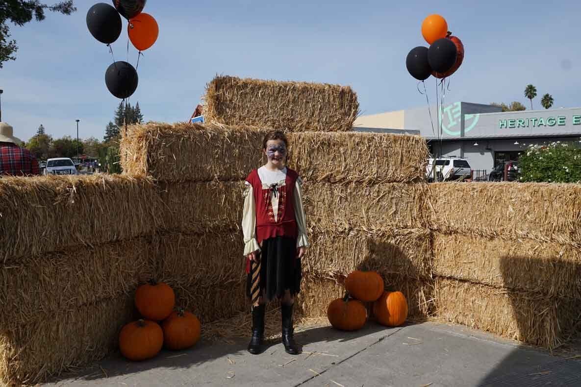 A person in a pirate costume is standing in front of hay bales and pumpkins.