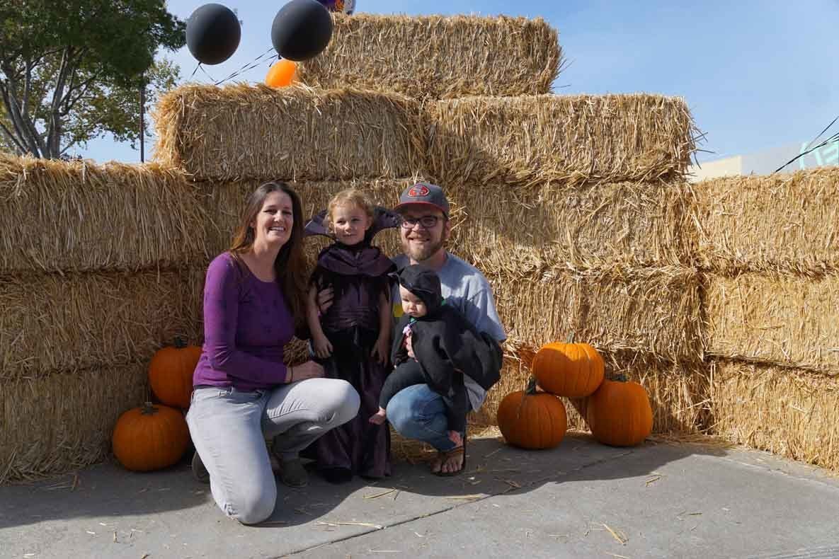 A family is posing for a picture in front of hay bales and pumpkins.