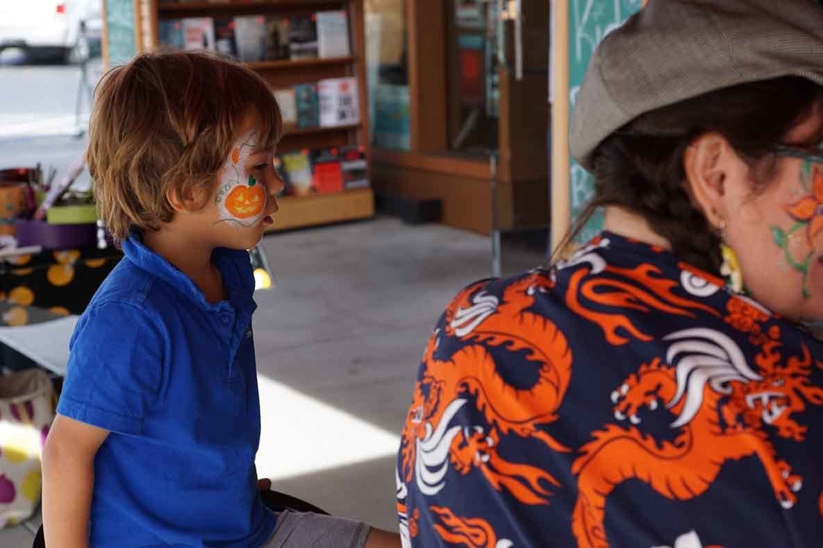 A boy with a face painted orange is sitting next to a woman with a dragon shirt on.