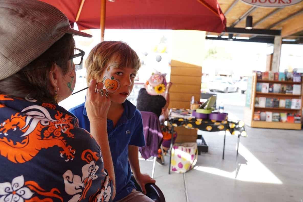 A woman is painting a child 's face in front of a book store