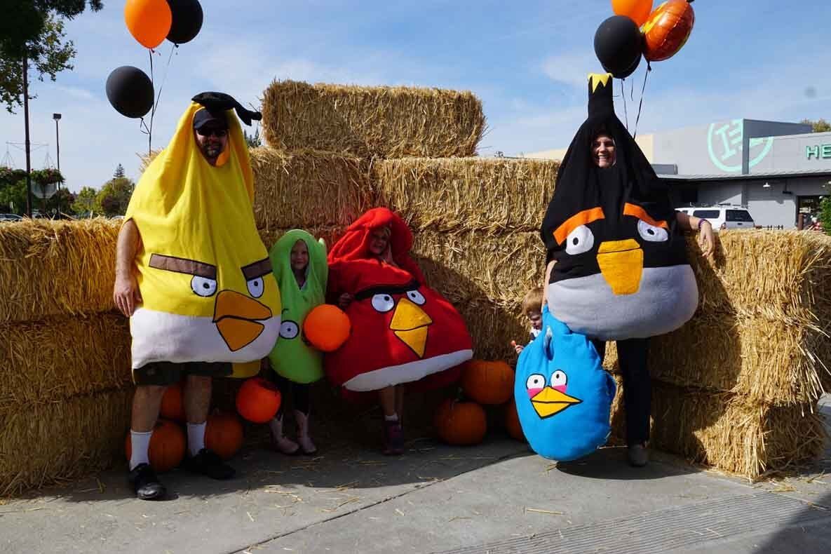 A group of people dressed in angry birds costumes are standing in front of hay bales.