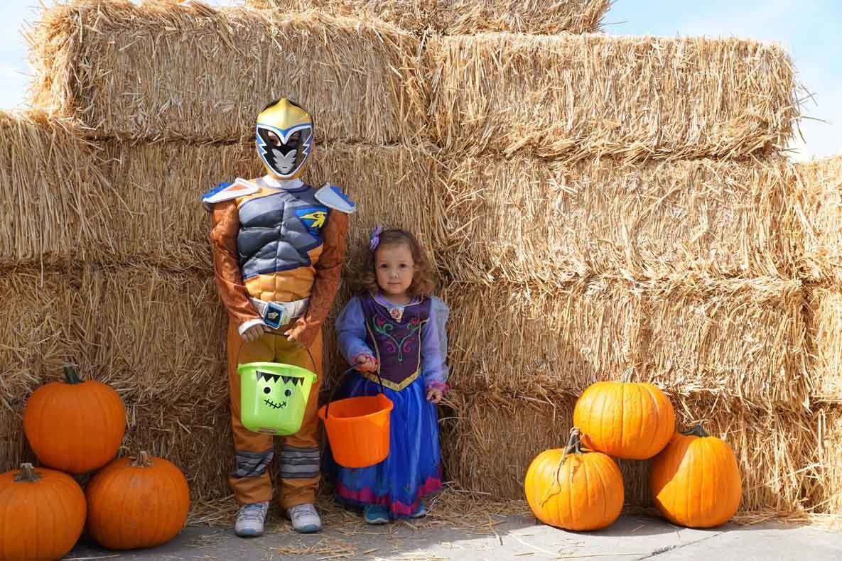A man and a little girl in costumes are standing next to a pile of hay.