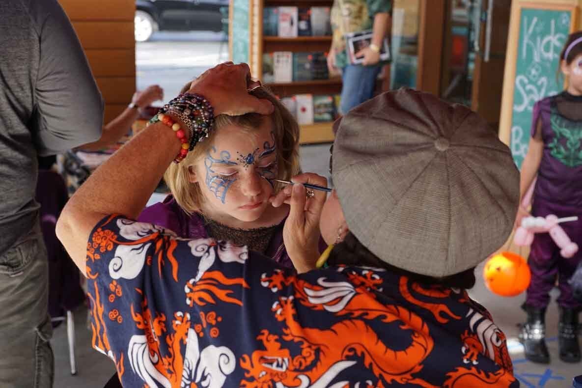 A girl is getting her face painted by a man.