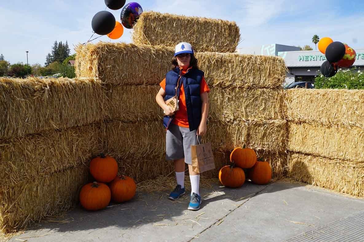 A man is standing in front of hay bales and pumpkins.