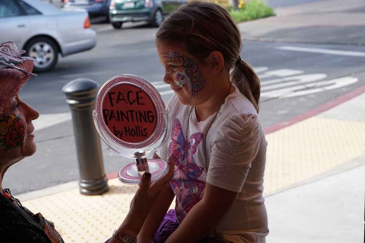 A little girl is getting her face painted by a woman.