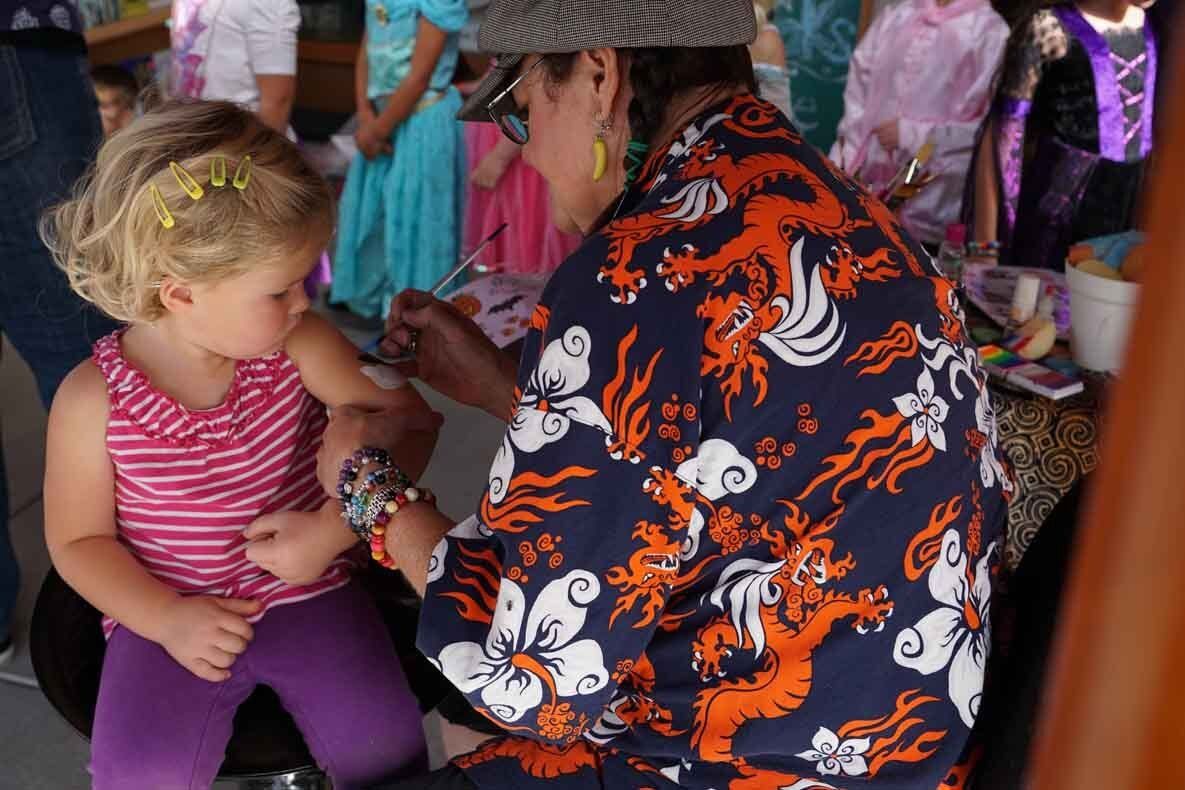 A woman in a hawaiian shirt is putting bracelets on a little girl 's arm.