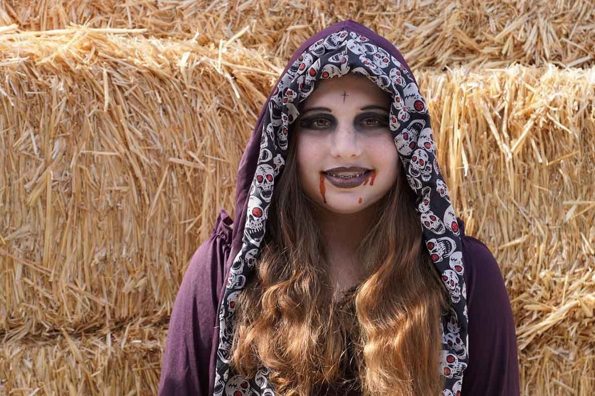 A woman in a vampire costume is standing in front of a hay bale.