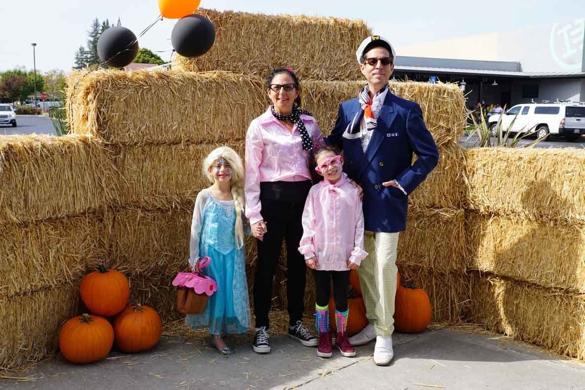 A family is posing for a picture in front of hay bales and pumpkins.