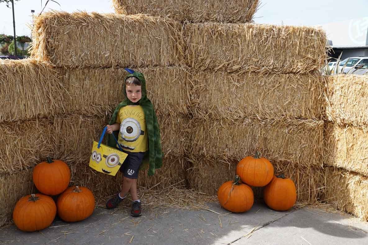 A young boy in a minion costume is standing next to a pile of hay bales.