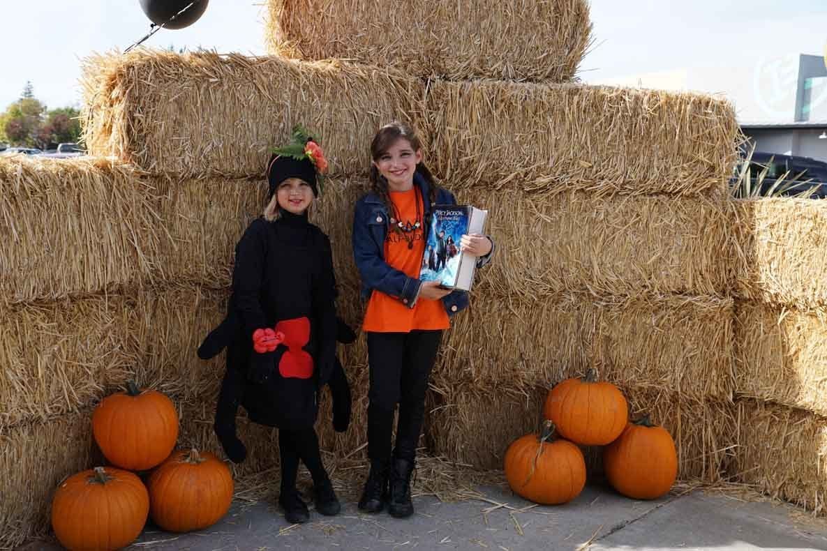 Two girls in halloween costumes are standing next to hay bales and pumpkins.