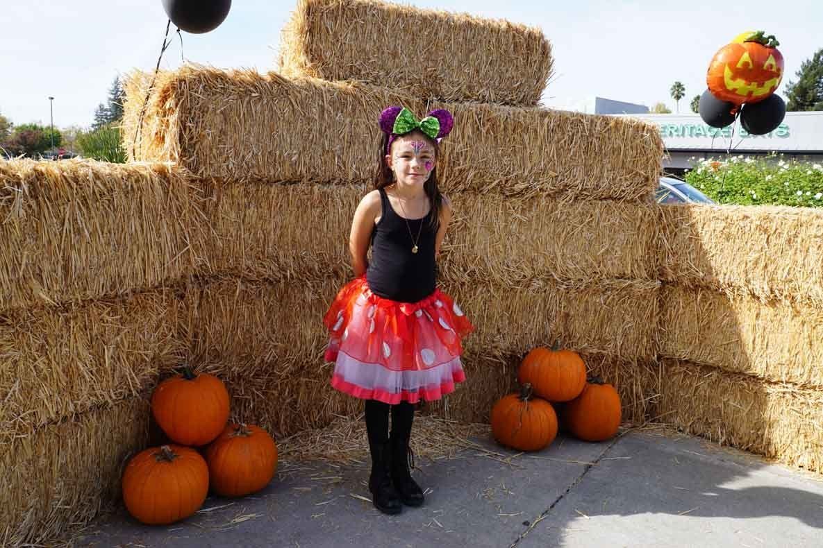 A little girl in a minnie mouse costume is standing in front of hay bales and pumpkins.